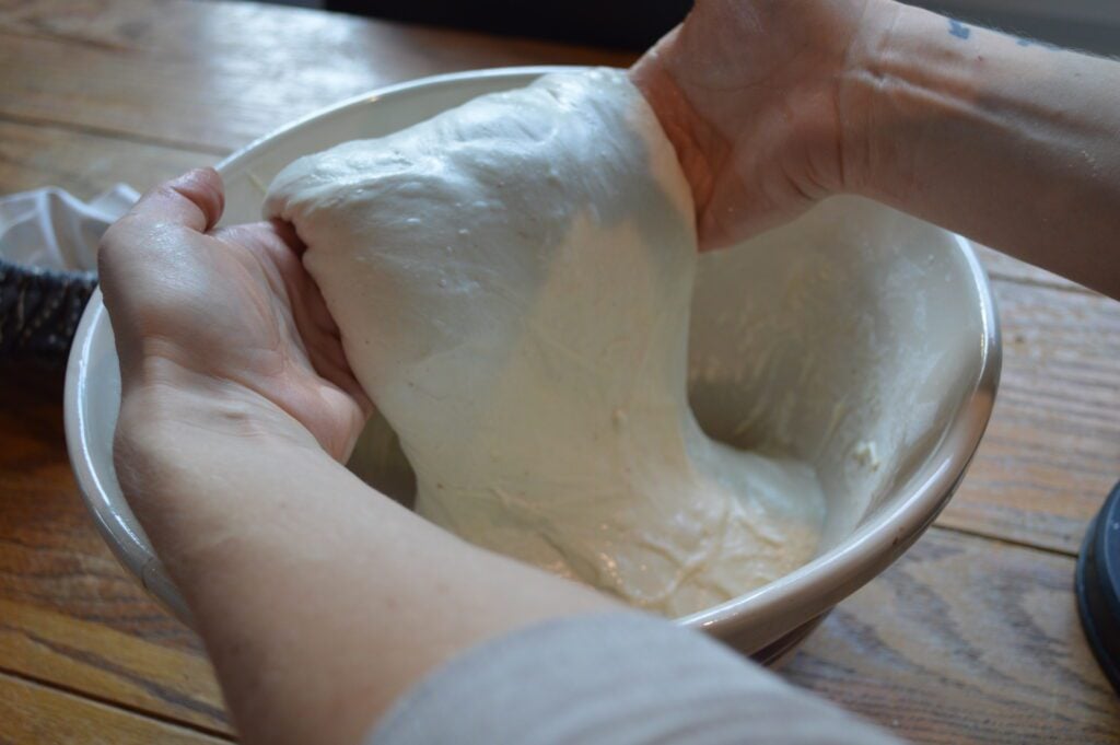 hands lifting sourdough dough up out of a bowl to fold over