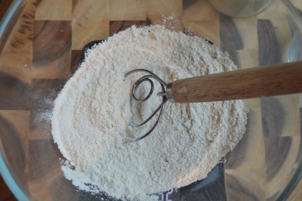 A bowl filled with flour, with a danish whisk in the bowl