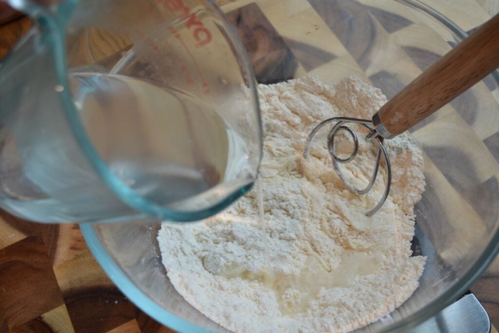 water being poured into mixing bowl of flour