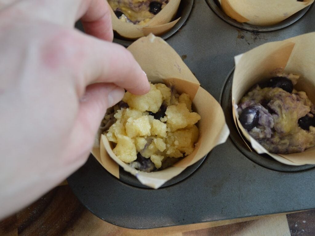 hand adding streusel topping to muffin batter