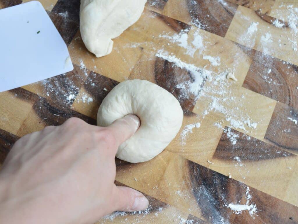 hand poking middle of sourdough bagel dough to shape it